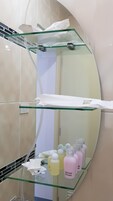 A bathroom with a curved mirror, glass shelves, and toiletries.