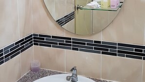A bathroom with a round mirror, a sink, and a glass shelf with toiletries. - Coffee Station Hostel (Udon Thani)