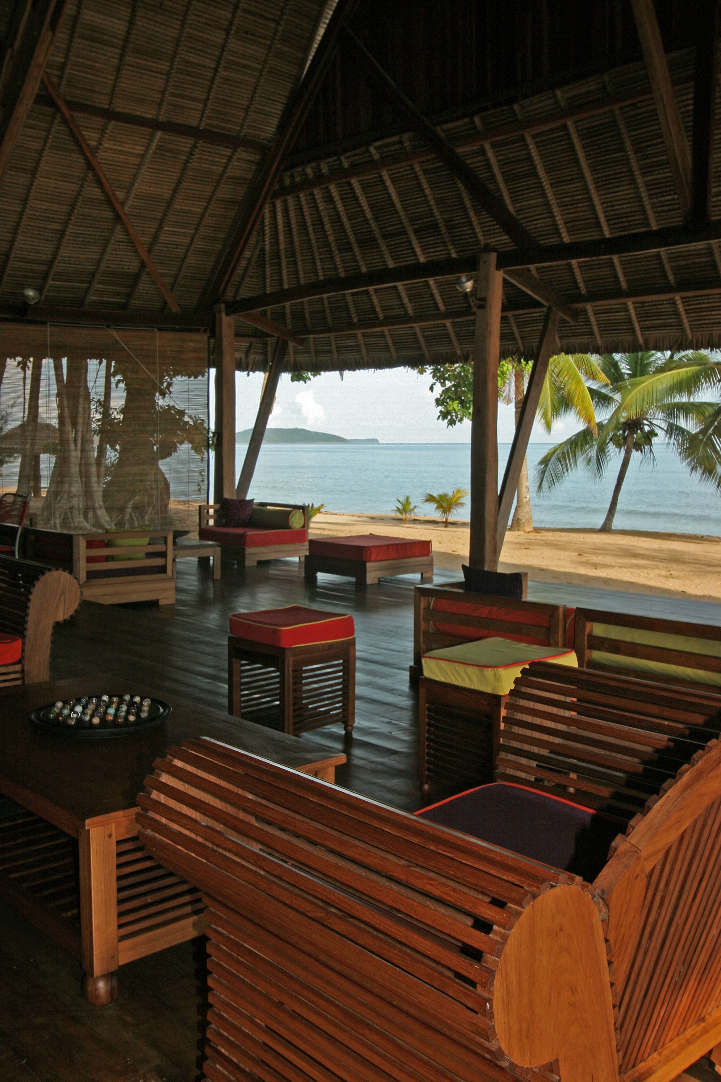 A covered outdoor seating area with wooden furniture and a view of the beach and ocean.