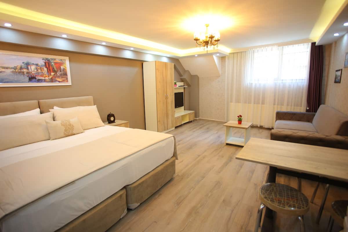 A hotel room with a large bed, a sofa, a dining table, and a TV.