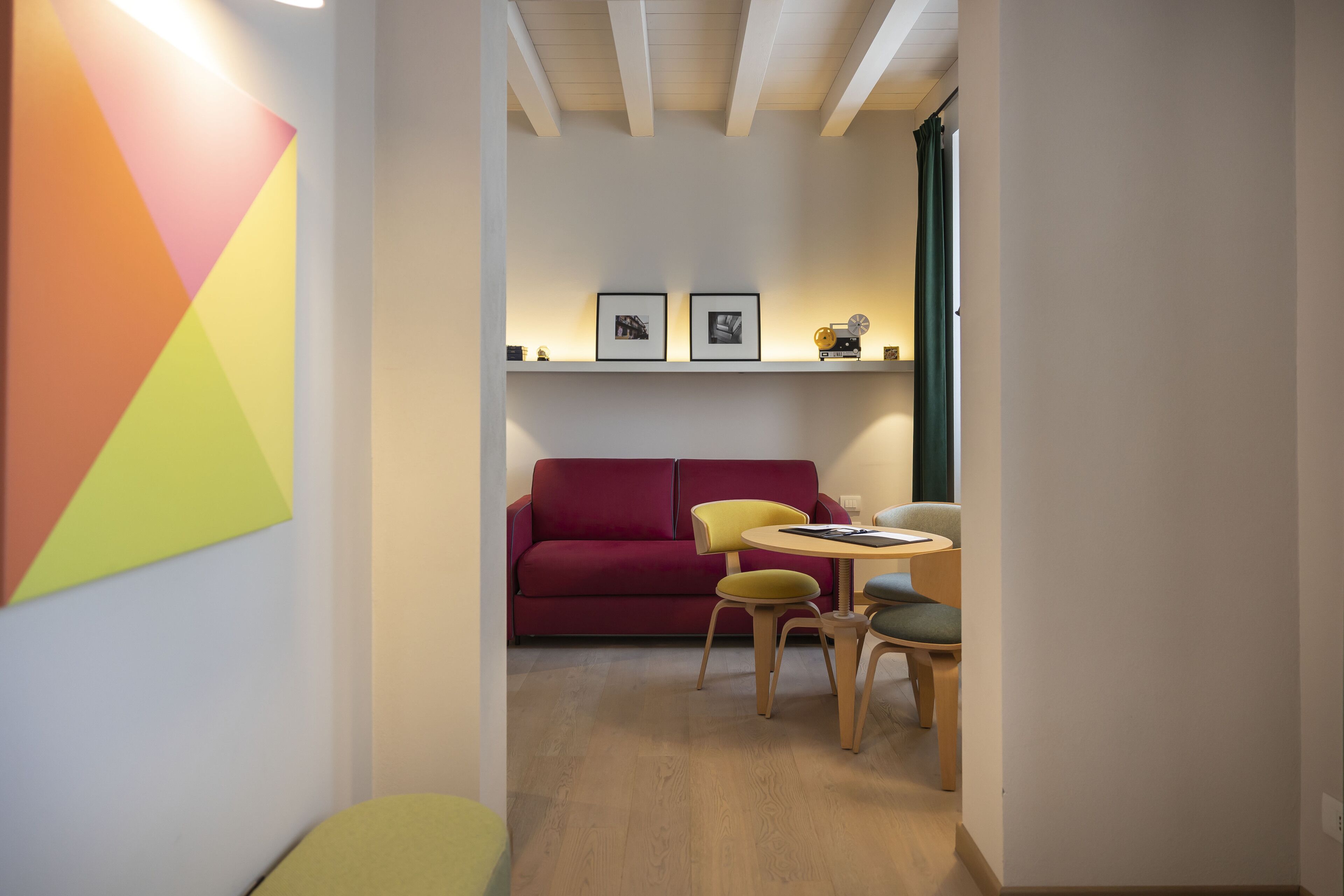 A modern living room with a red sofa, yellow and green chairs, a small round table, and two framed pictures on the wall.