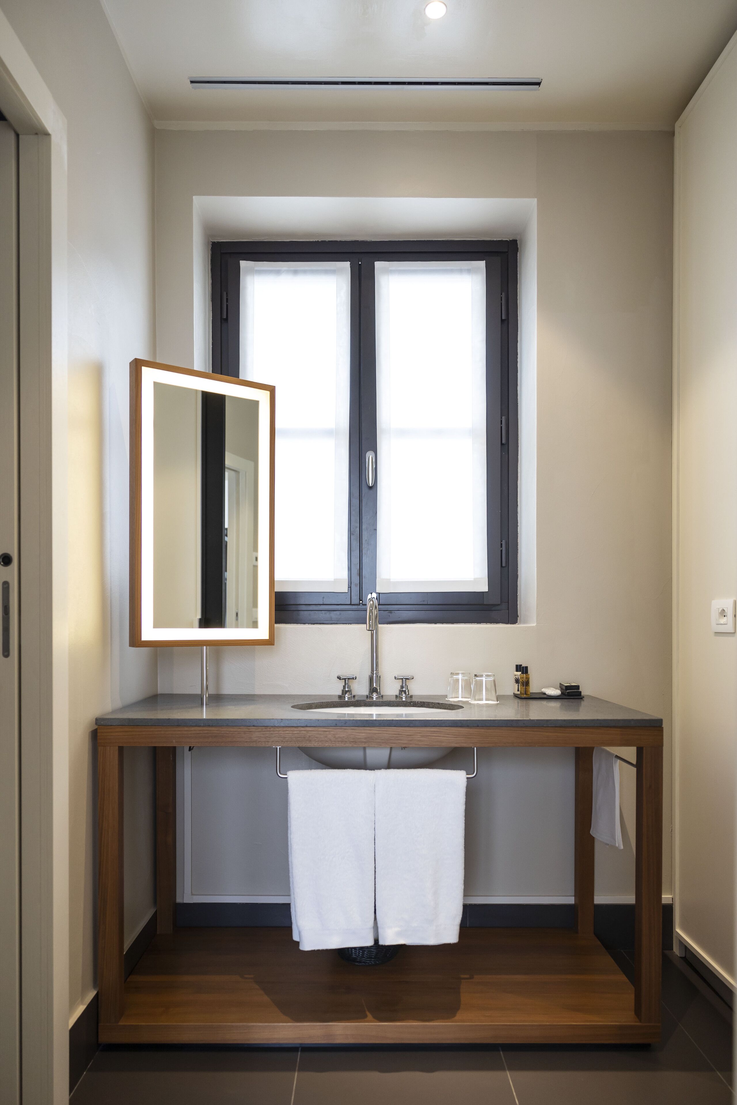 A modern bathroom with a wooden vanity, a large mirror, a window, and a towel rack.