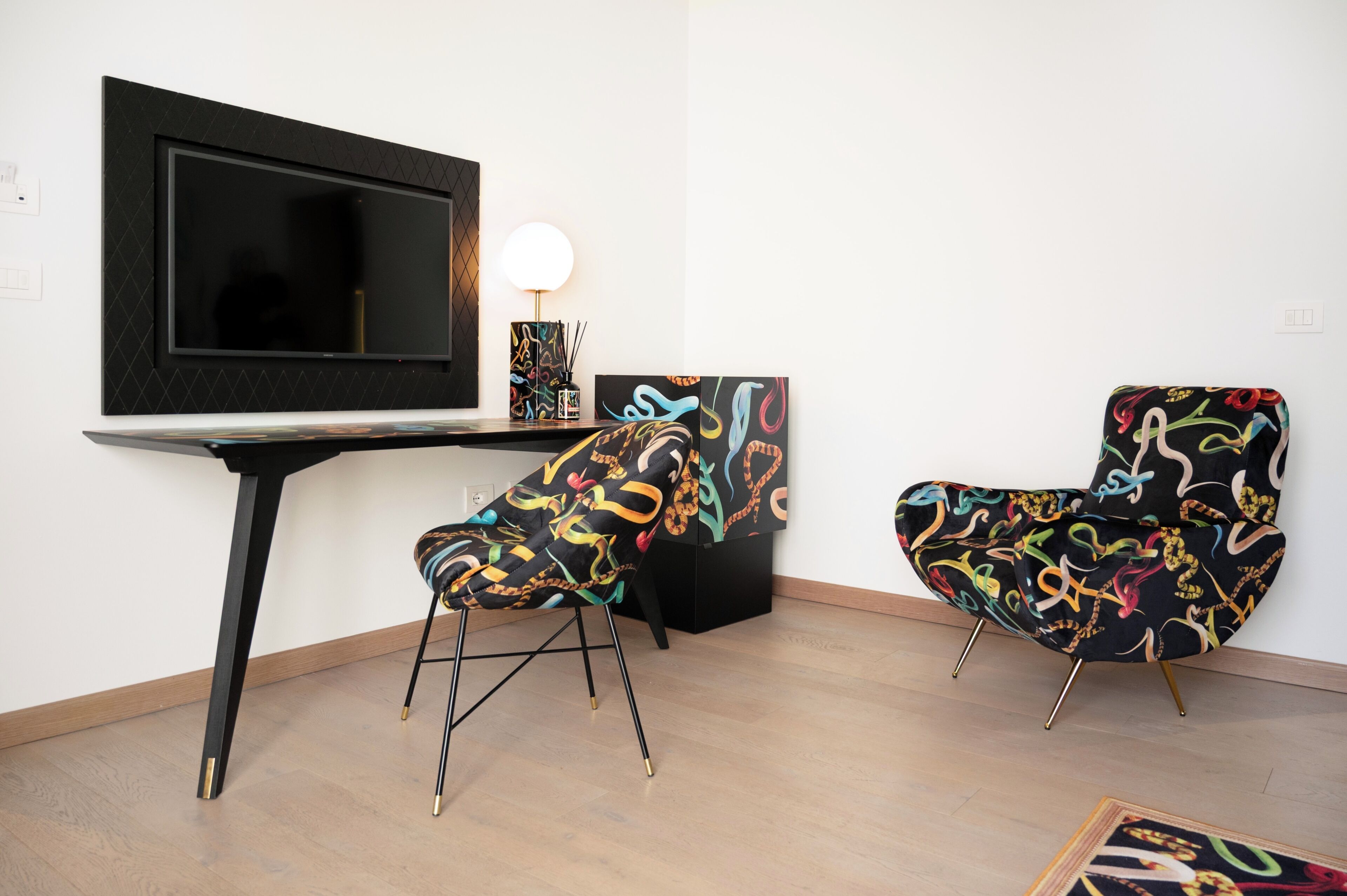 Una habitación moderna con televisión de pantalla plana, dos sillones estampados, una mesita con lámpara y arte abstracto en la pared.