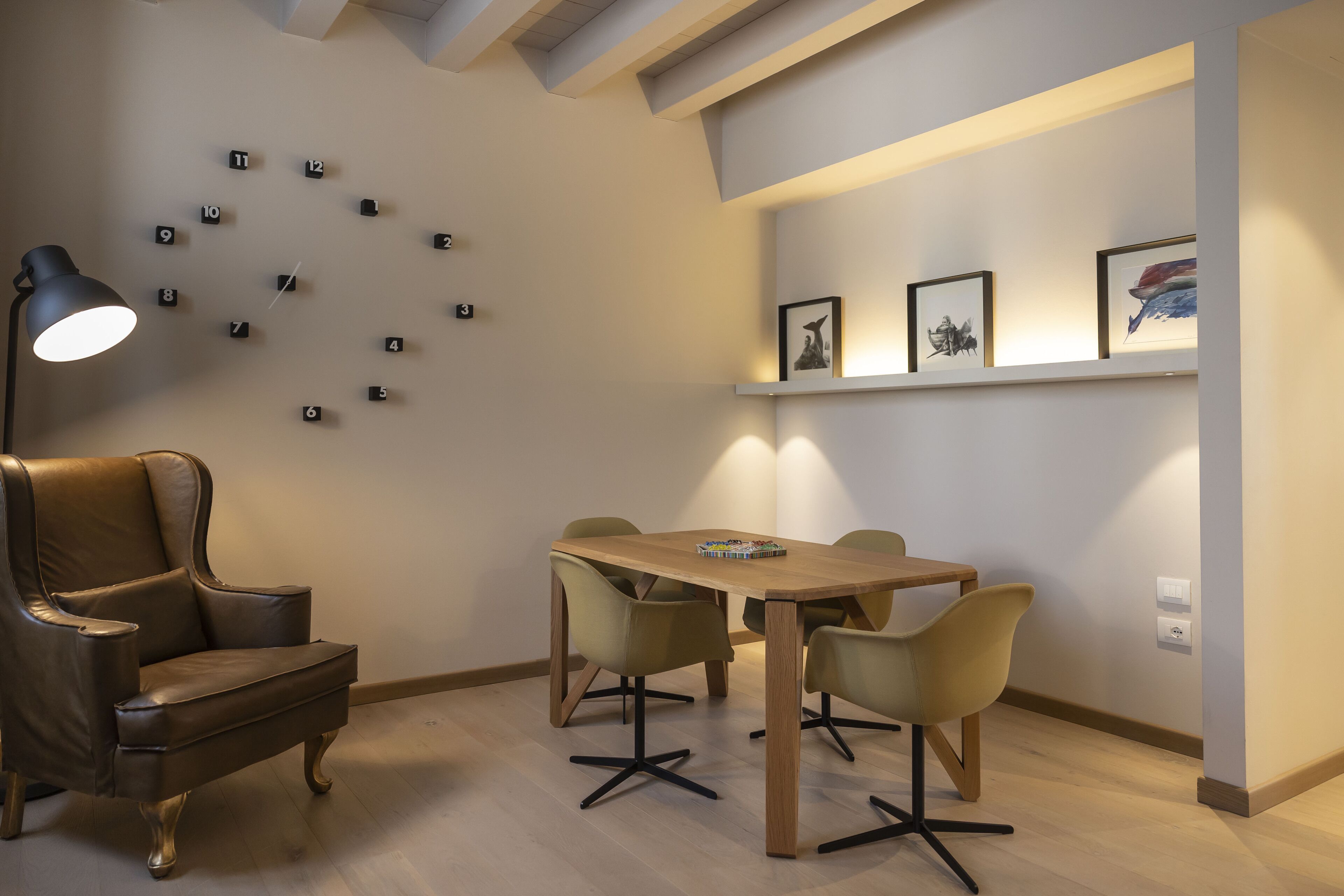 Uma sala de jantar moderna com mesa e cadeiras de madeira, uma poltrona de couro e um relógio na parede.