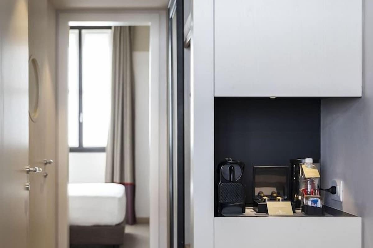 Una habitación de hotel compacta con kitchenette, una cama y un ventanal con cortinas.