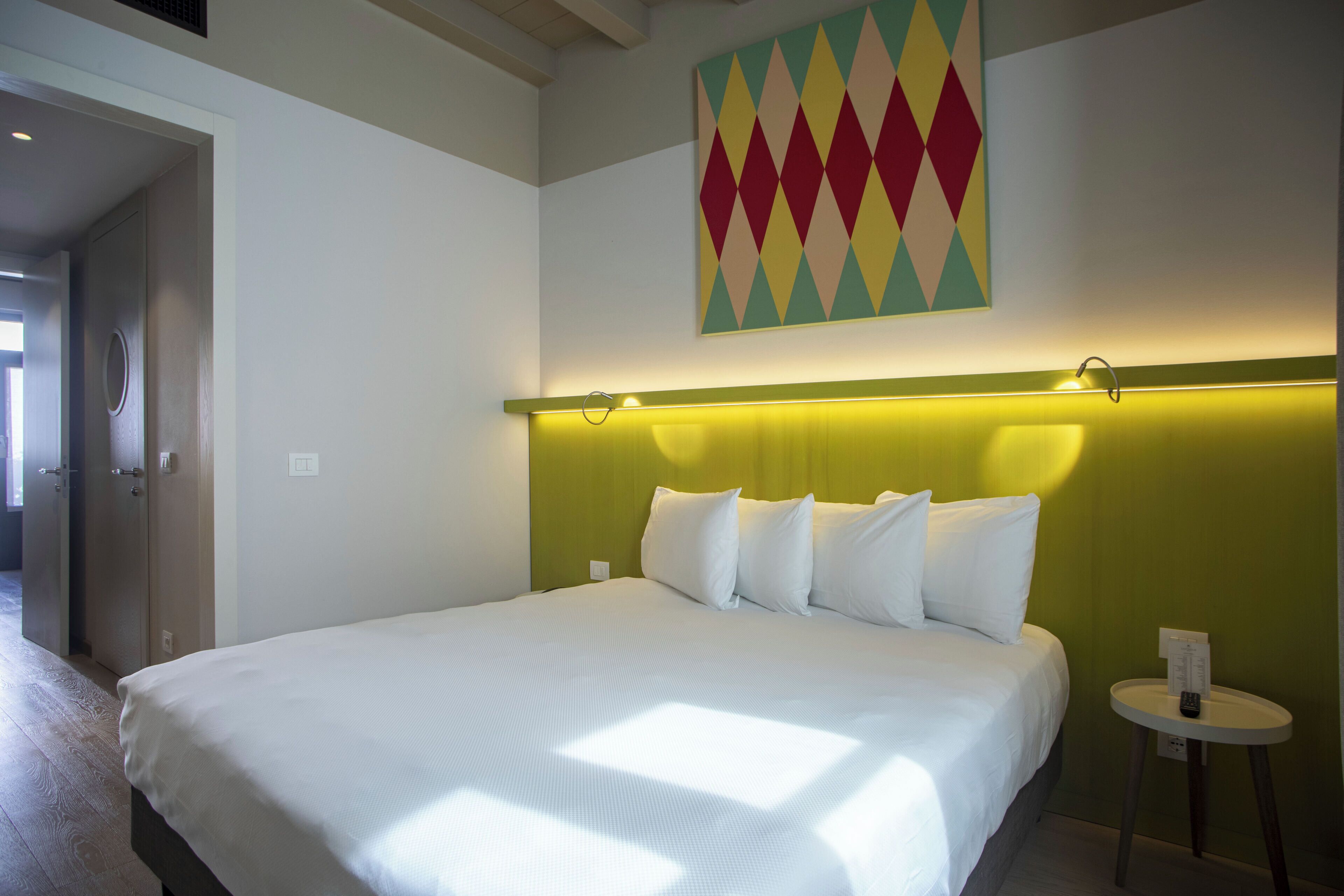 A hotel room with a large bed, a green accent wall, and a colorful artwork above the bed.