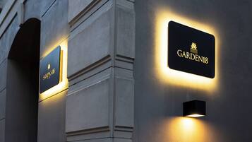 Beleuchtete Schilder an der Fassade eines Gebäudes, darunter ein Schild mit der Aufschrift "GARDEN18".