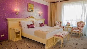 A hotel room with a large bed, a nightstand, a chair, and a small table.