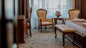 Habitación de hotel con una cama, dos sillones tapizados, una mesita redonda con un florero y un banco.