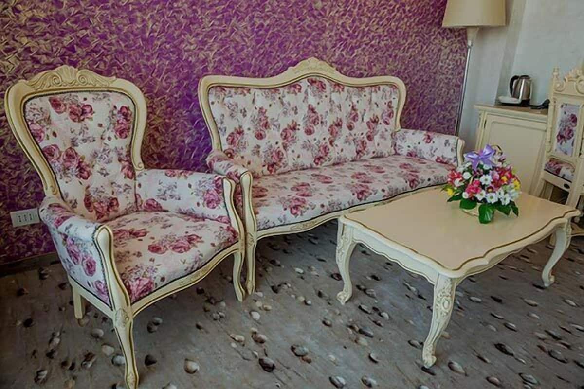 A room with a floral sofa and a matching armchair, a small table with a vase of flowers, and a patterned carpet.