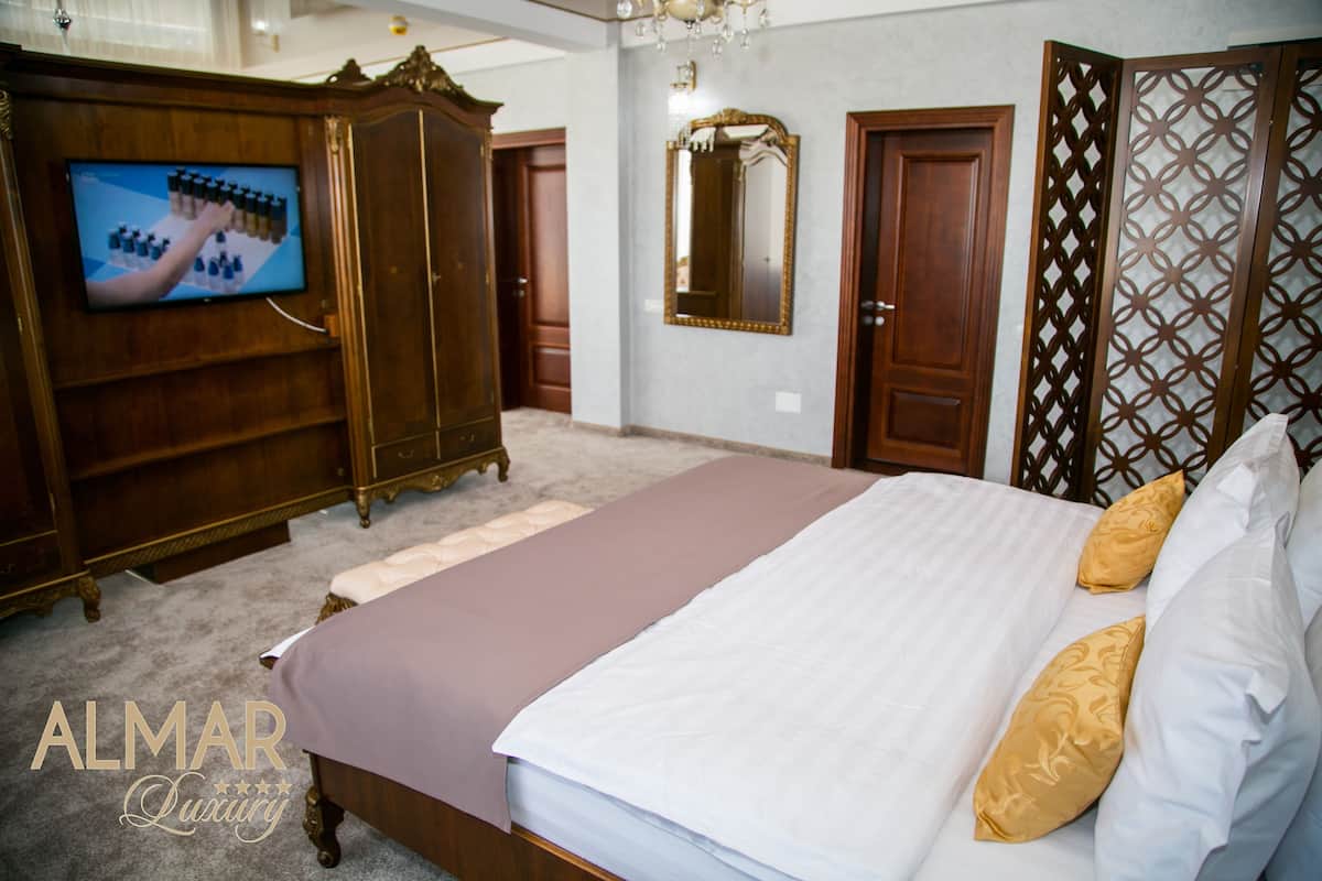 A bedroom with a large bed, a television, a wardrobe, and a mirror.