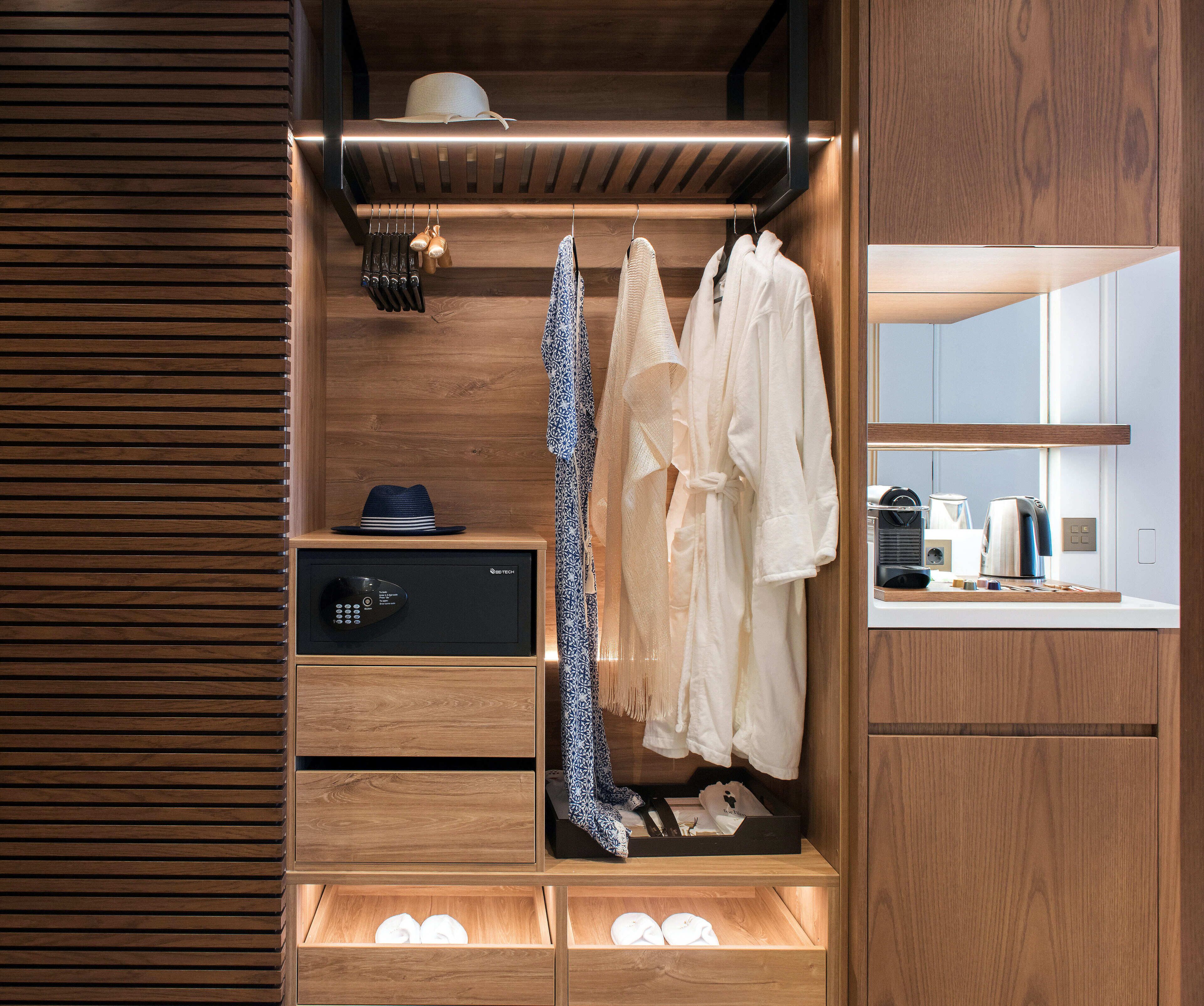 A wooden wardrobe with a built-in microwave, hanging robes, and neatly folded towels.