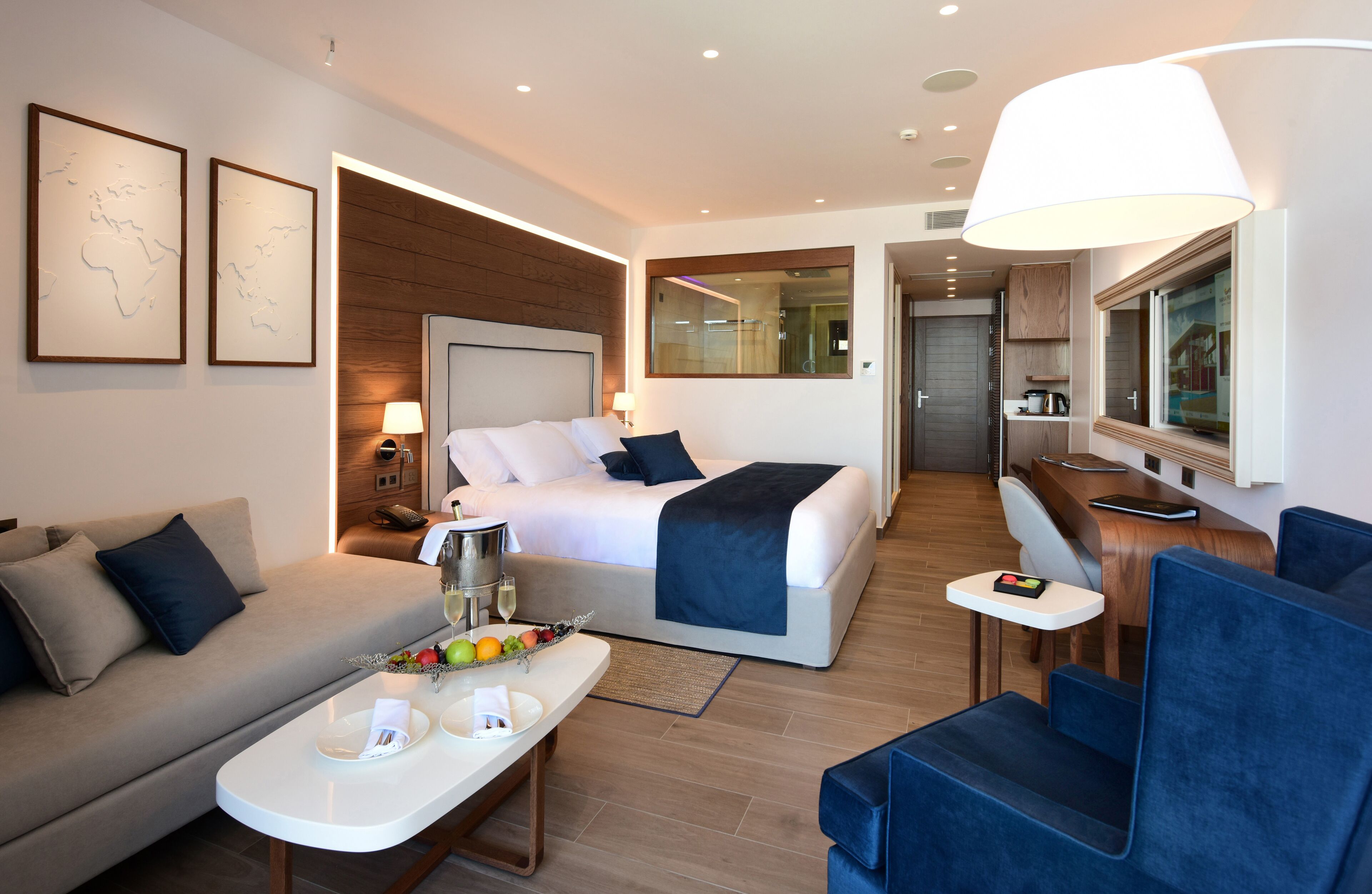Una habitación de hotel moderna con una cama, un sofá, una mesa de comedor con fruta, un escritorio y un gran ventanal.