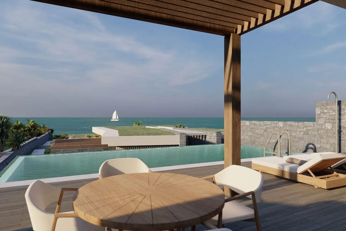 A poolside area with a view of the sea, a sailboat, and a stone wall.
