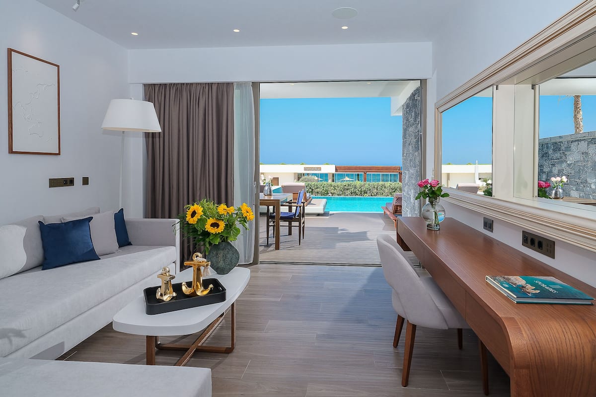 A modern hotel room with a sofa, coffee table, and a view of the pool and ocean.