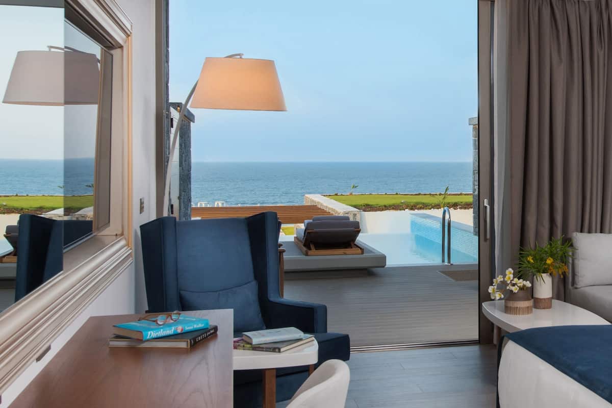A modern room with a view of the sea, a pool, and a balcony with seating.
