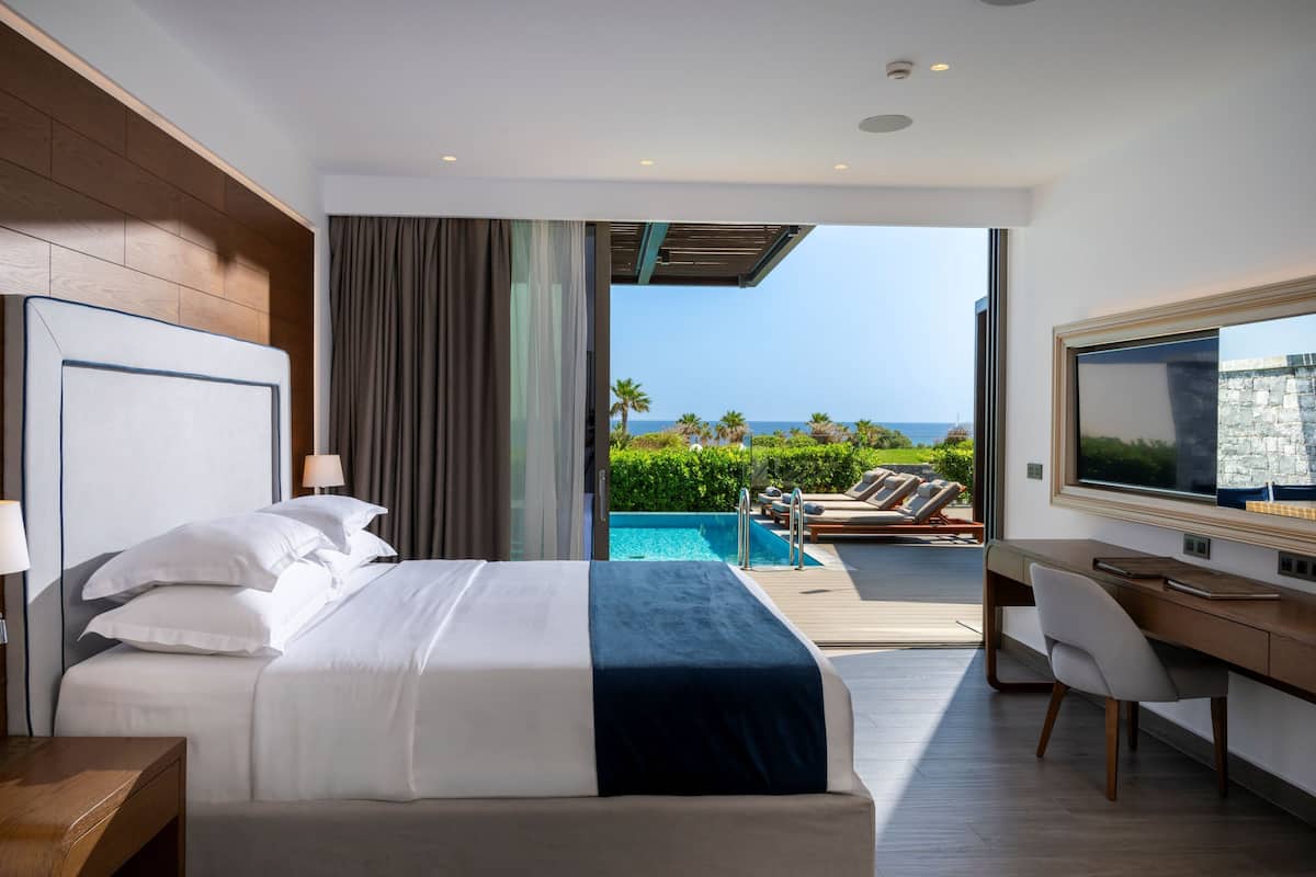 A modern hotel room with a large bed, a desk, and a view of the ocean.