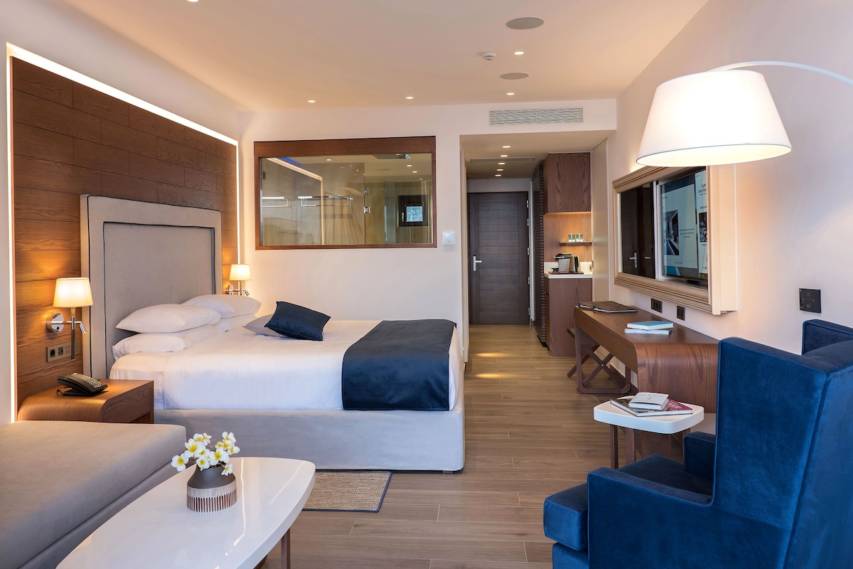 Une chambre d’hôtel comprenant un lit, une table de chevet, une lampe, un bureau, une chaise et un miroir.
