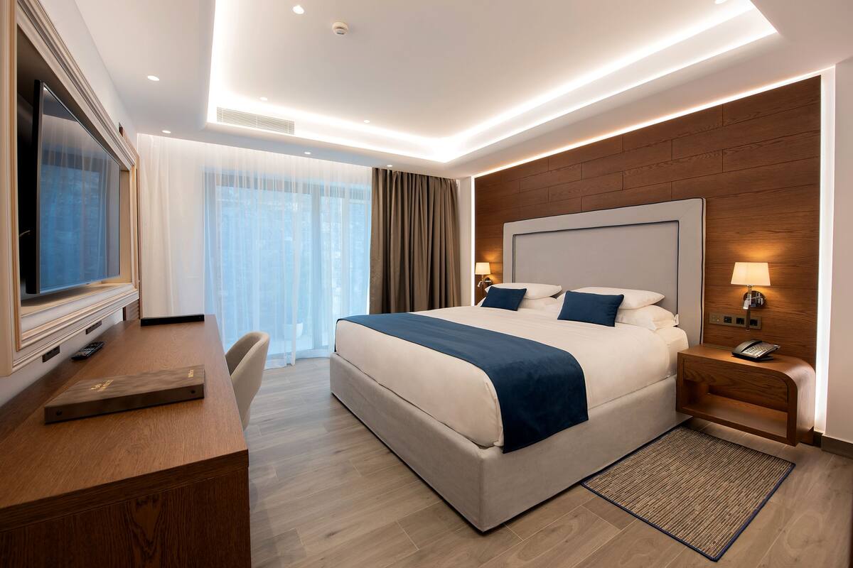 A modern hotel room with a large bed, a desk, a television, and a view of the outdoors.