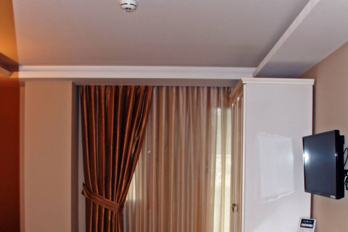 Habitación de hotel con cama, escritorio, silla, televisor y ventana con cortinas.