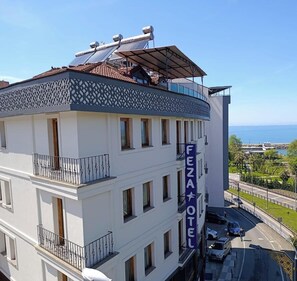 Un hôtel à plusieurs étages doté de balcons, d’un toit-terrasse équipé de panneaux solaires et offrant une vue sur la mer.