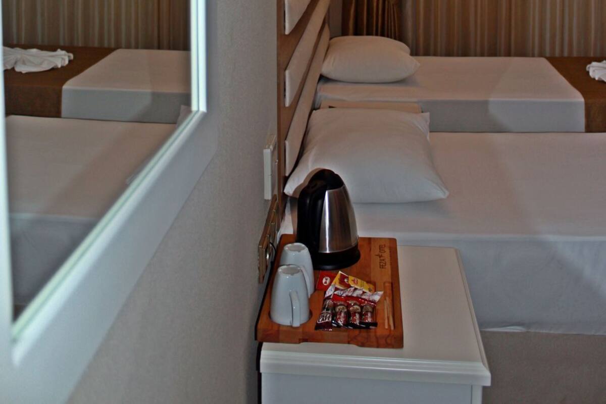 Habitación de hotel con cama, mesita de noche con tetera, taza y aperitivos, además de una lámpara de pared.