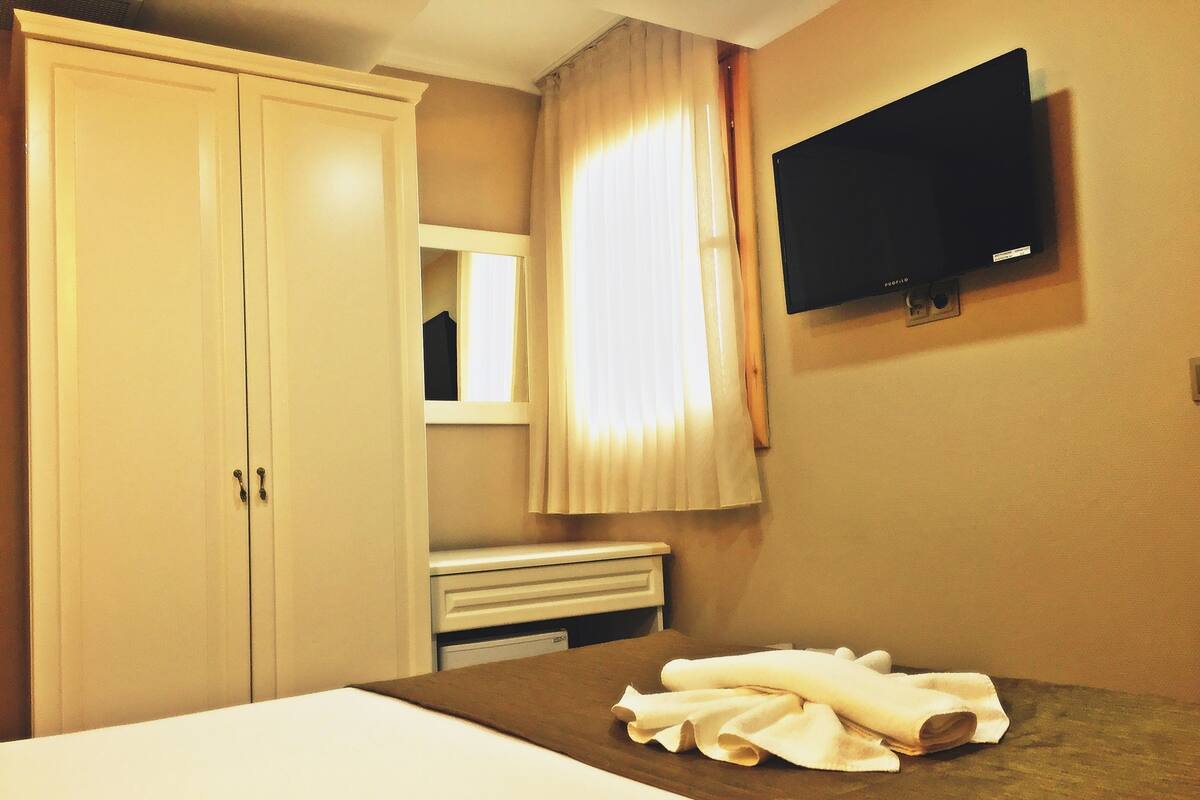 Una habitación de hotel con cama, televisión, armario y ventana con cortinas.