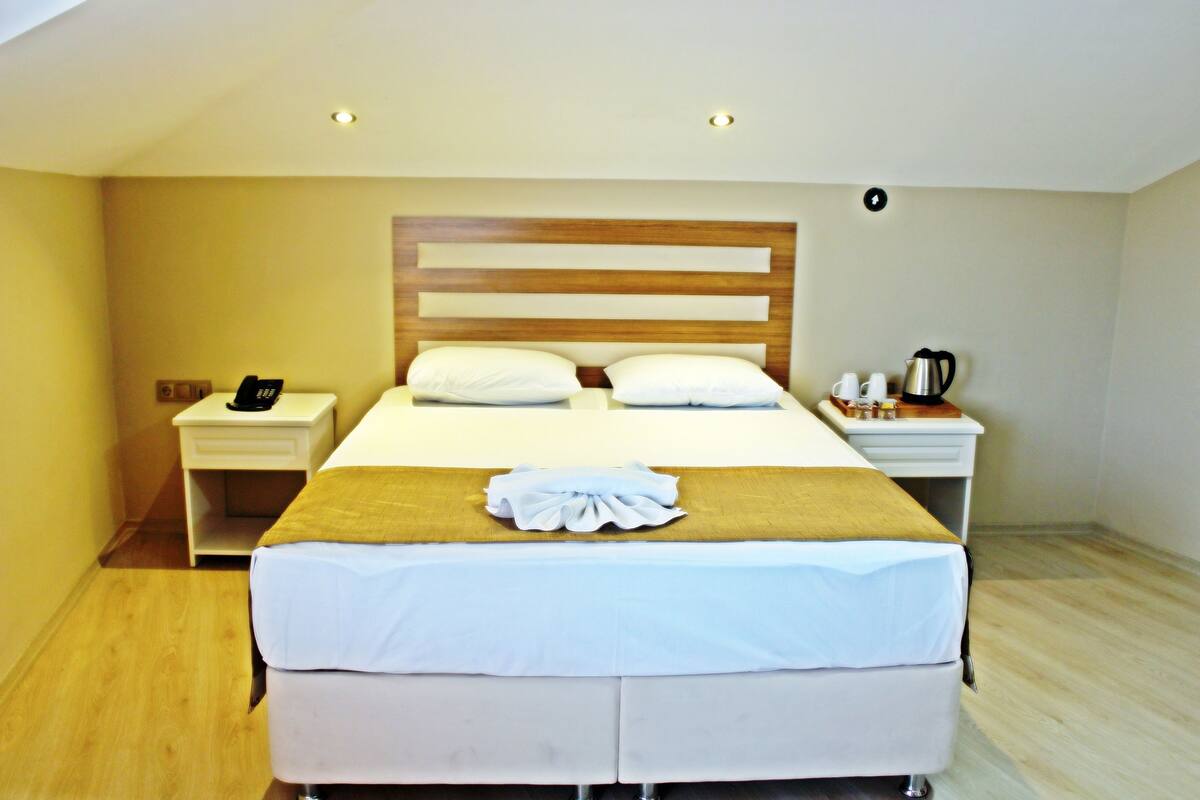 Una habitación de hotel con cama, mesitas de noche, cafetera y una lámpara de pared.