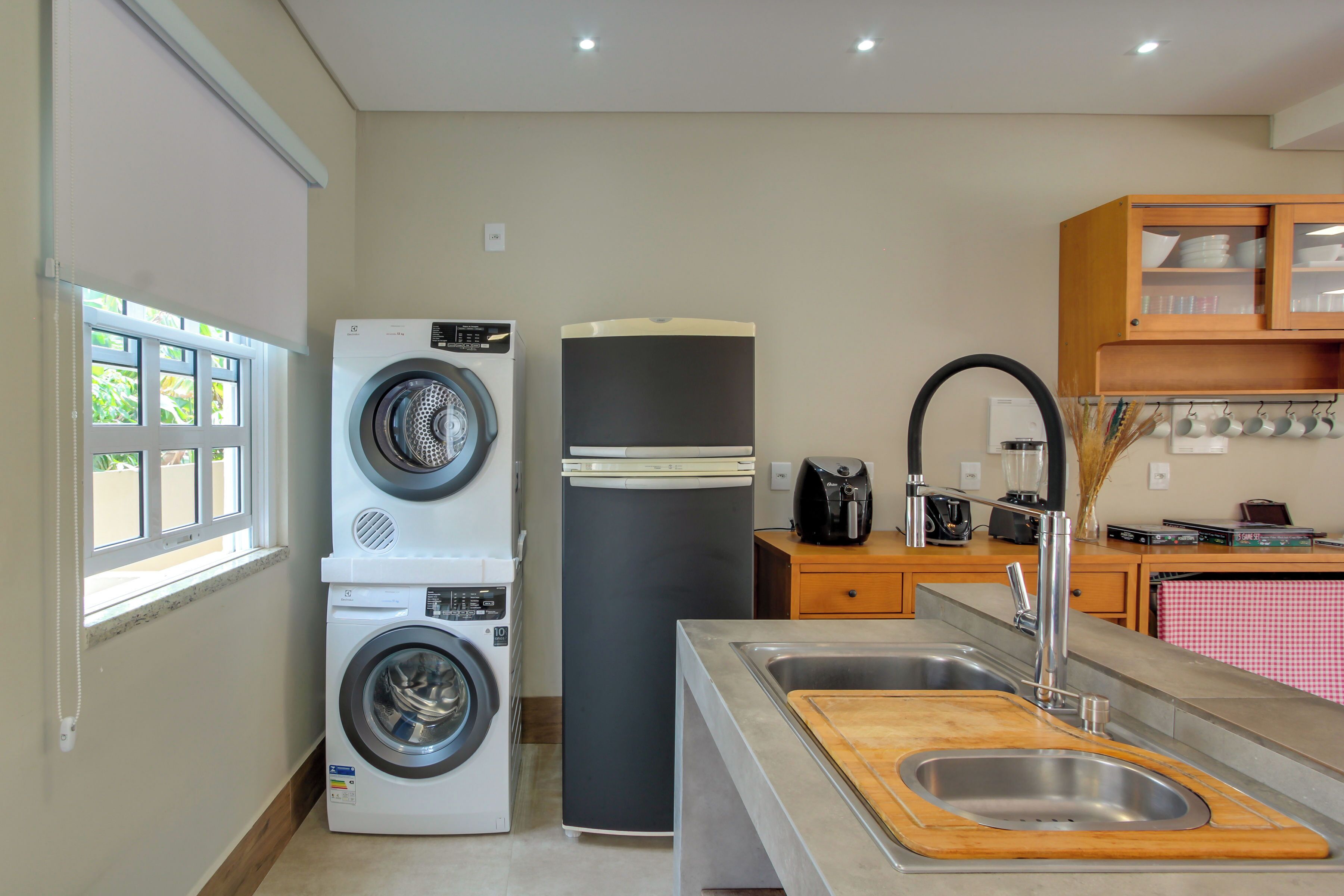 Une cuisine compacte équipée d’un lave-linge, d’un réfrigérateur, d’un évier avec une planche à découper en bois et d’un meuble contenant de la vaisselle.
