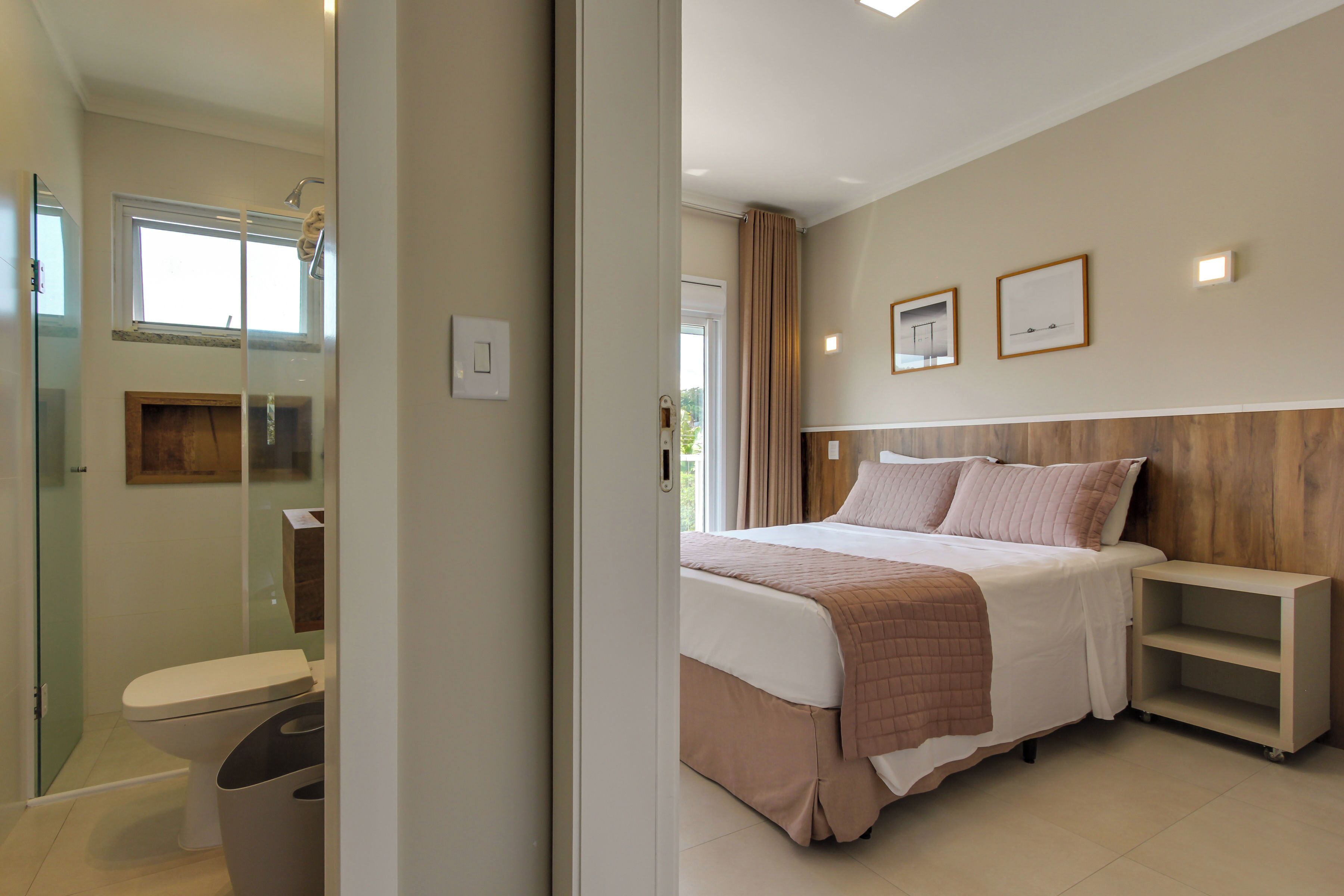 A modern hotel room with a large bed, a bedside table, a small shelf, and a shower area.
