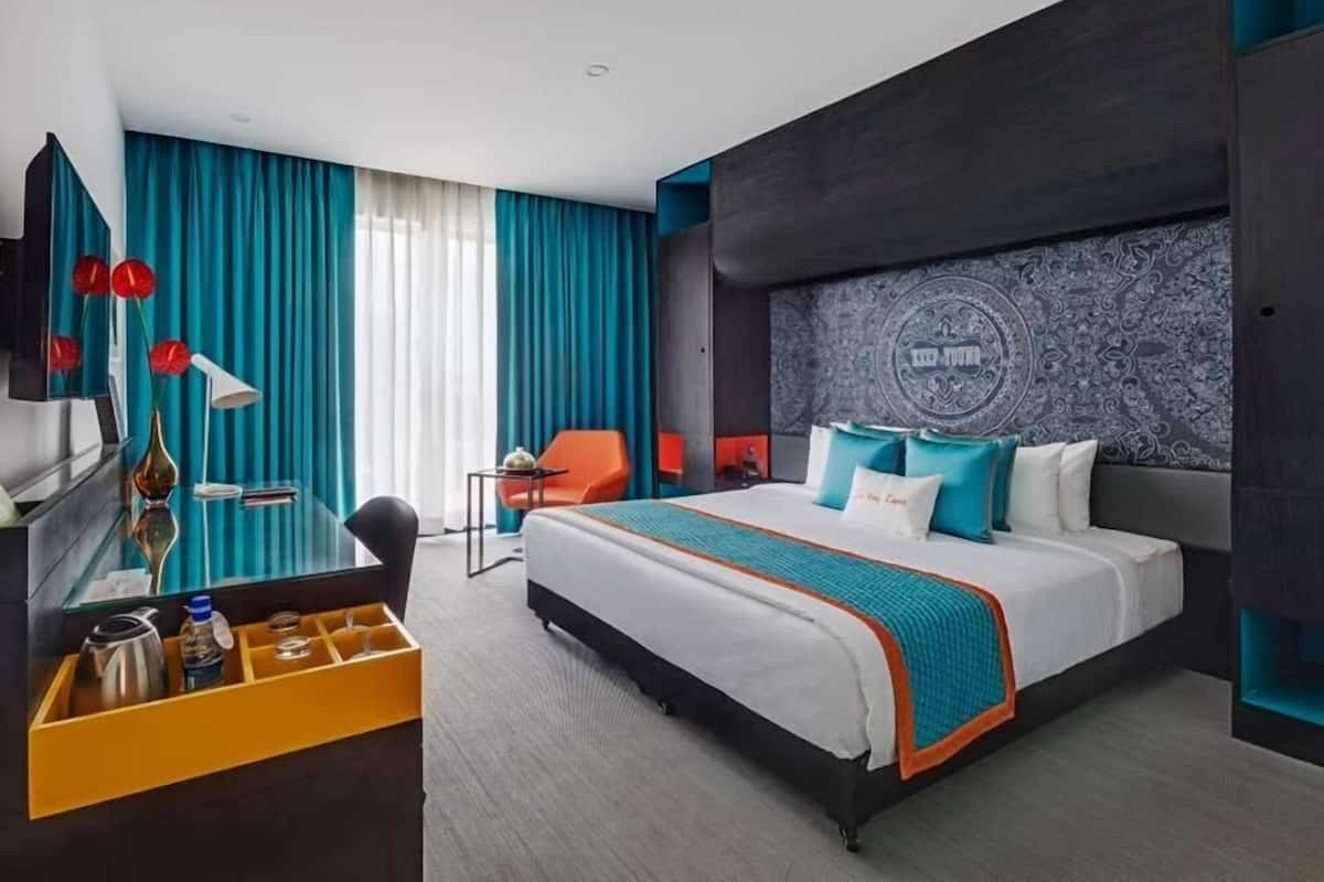 Quarto de hotel moderno com uma cama grande, uma escrivaninha com cadeira e uma televisão.