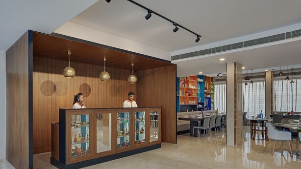 Een hotel receptie met een houten balie, glazen vitrines en een zithoek met tafels en stoelen.
