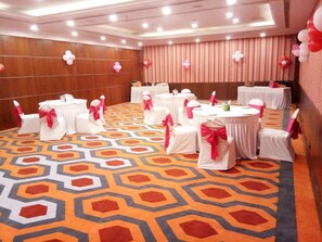 Uma sala de conferência com mesas redondas, cadeiras brancas com fitas cor-de-rosa e um tapete estampado.