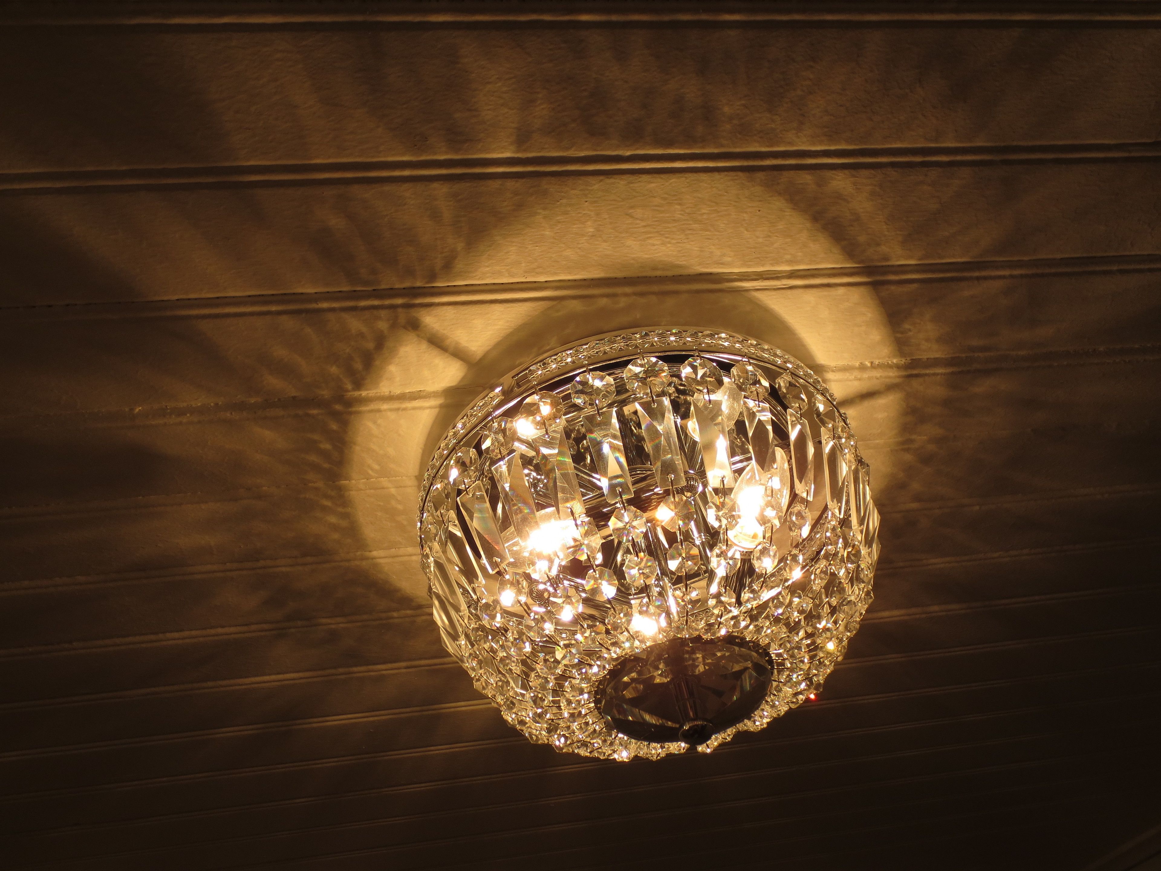 Ein Kristallluster mit mehreren Lichtquellen, an einer Wand mit horizontalen Linien befestigt.