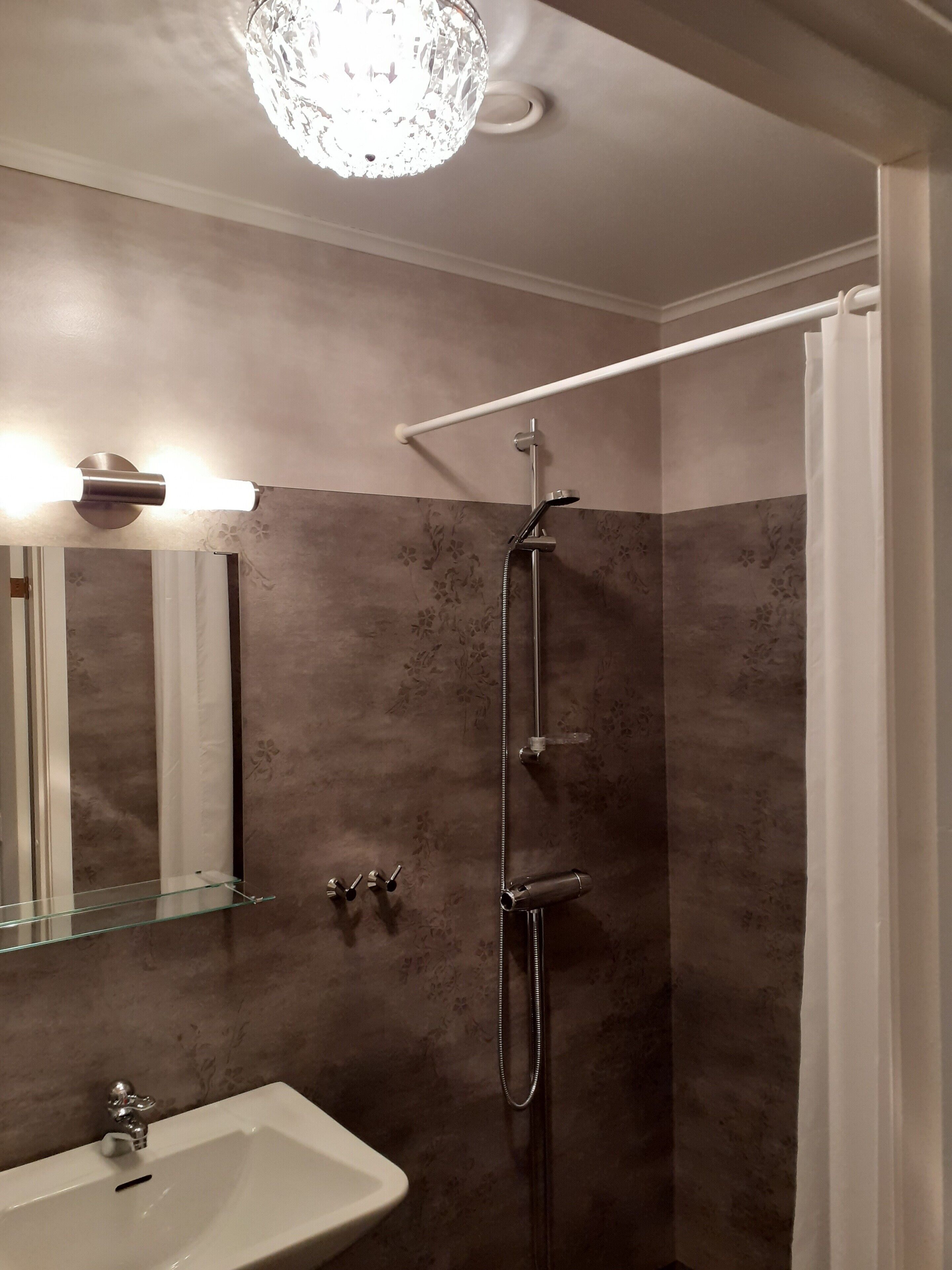 A modern bathroom with a glass shelf, a shower with a handheld showerhead, and a wall-mounted light fixture.