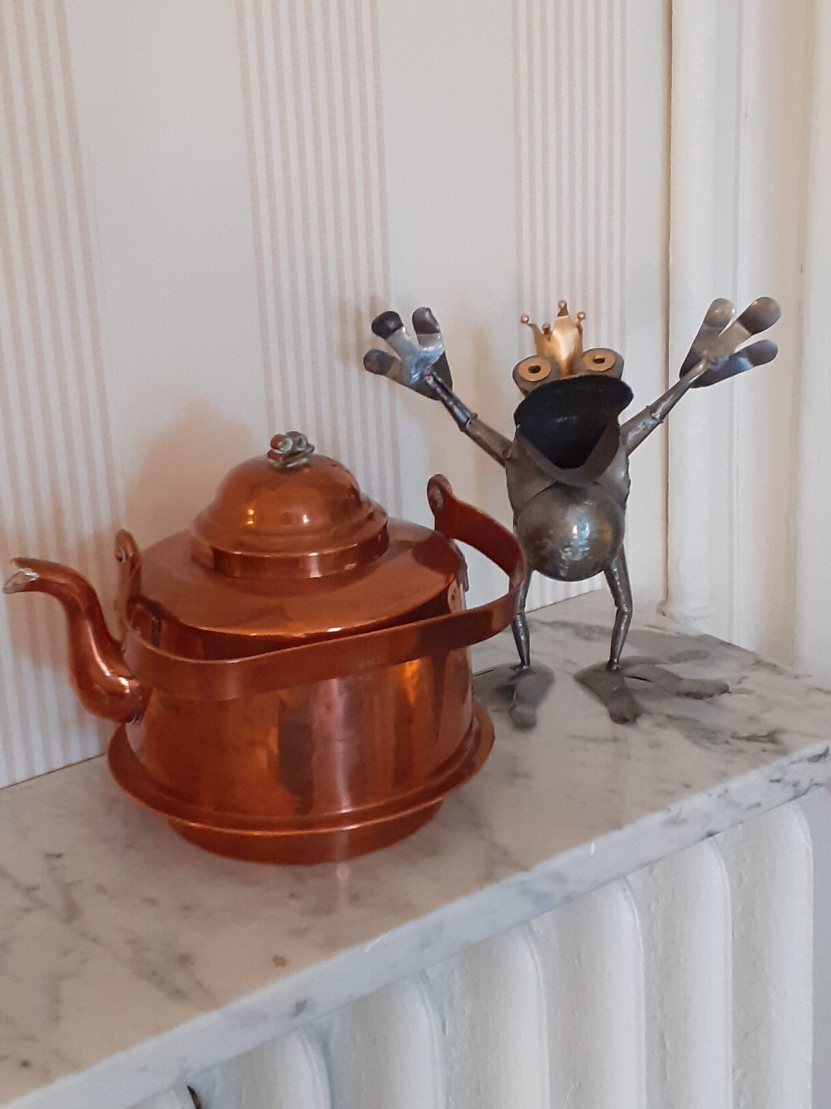 A copper teapot and a metal figurine on a marble shelf against a white wall.