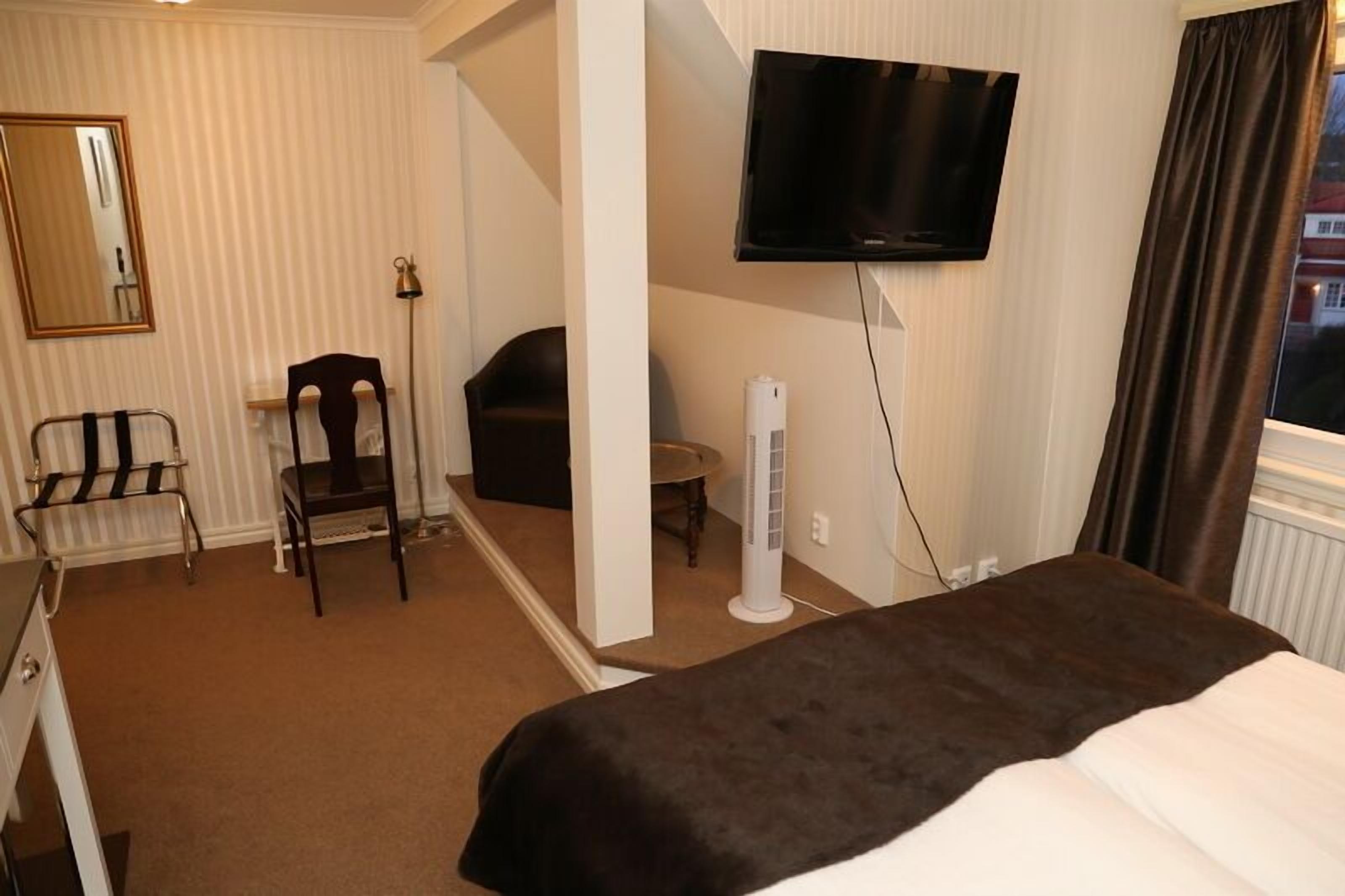 A hotel room with a bed, a chair, a desk, a television, and a window with curtains.