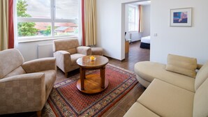 Una sala de estar moderna con un sofá, sillones, una mesa de centro y vistas a un paisaje urbano a través de amplios ventanales.
