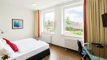 A hotel room with a bed, a desk with a chair, a TV, and large windows with curtains.