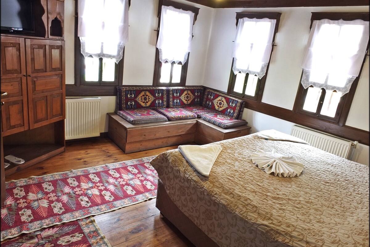 A bedroom with a large bed, a built-in bench with cushions, a wooden wardrobe, and a radiator.