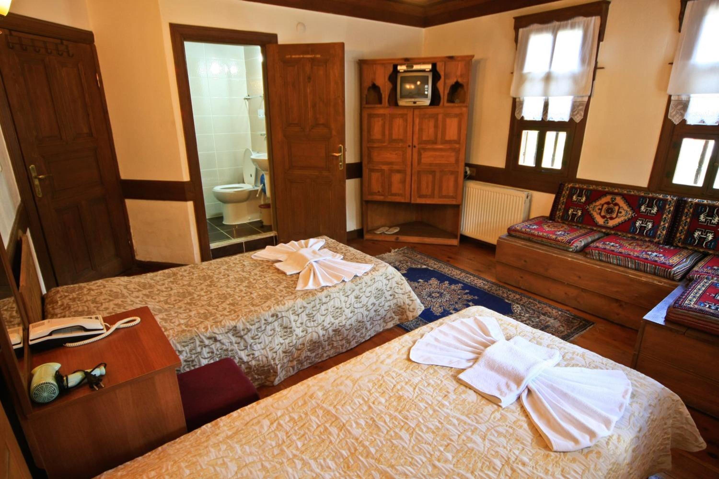 Quarto com duas camas, um guarda-roupa de madeira, uma televisão e um sofá com almofadas estampadas.