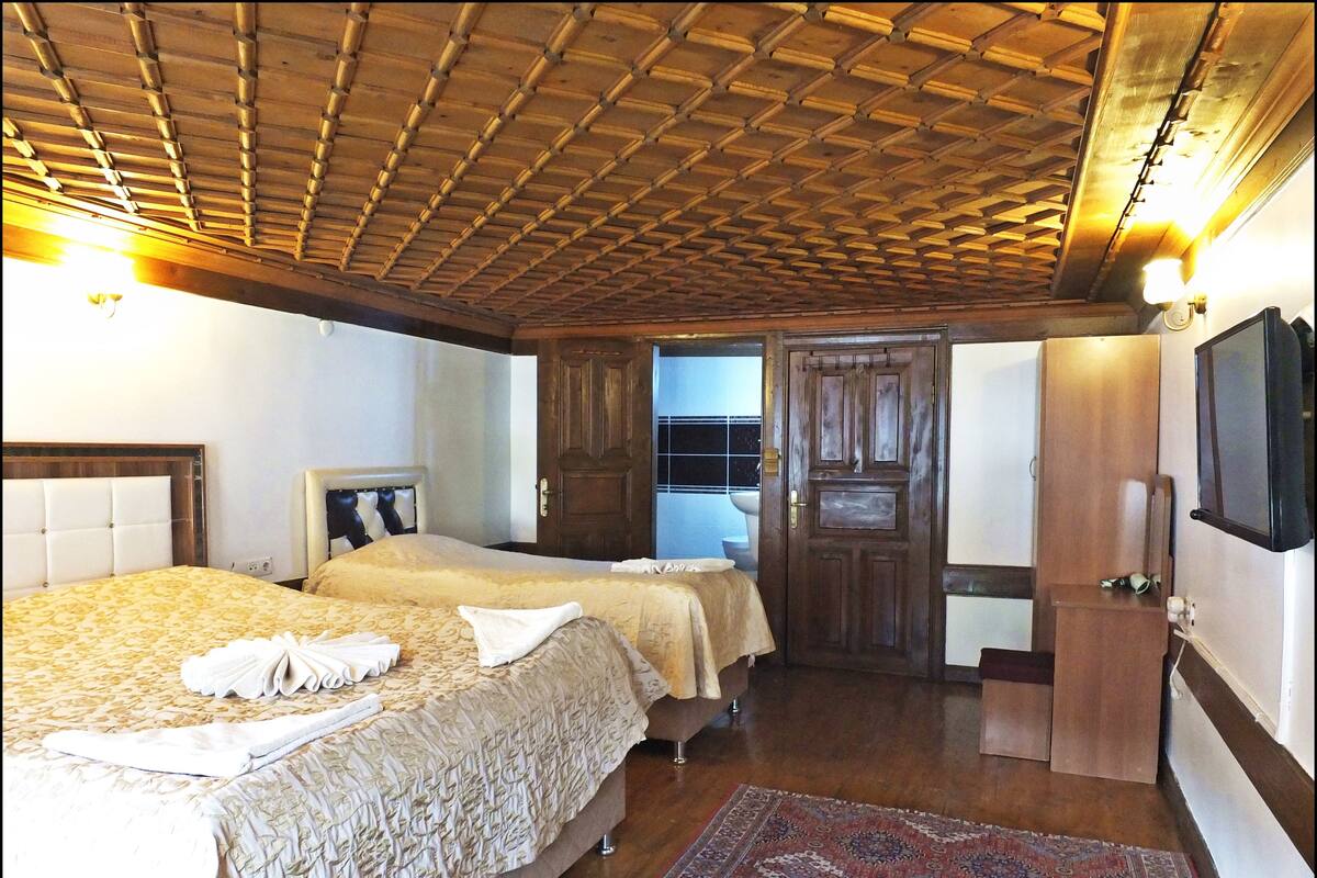 A hotel room with two beds, a wooden ceiling, a large mirror, and a TV on the wall.