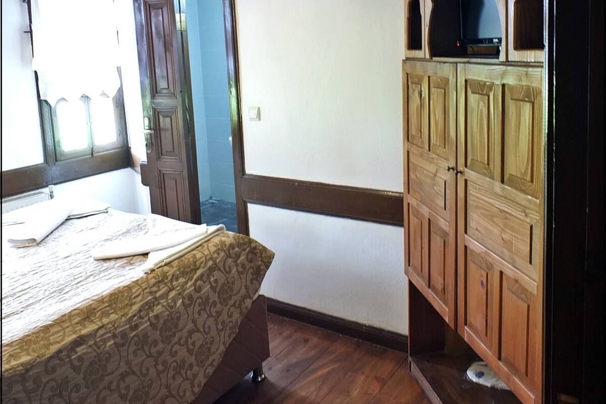A room with a bed, wooden wardrobe, and a door leading to another room.