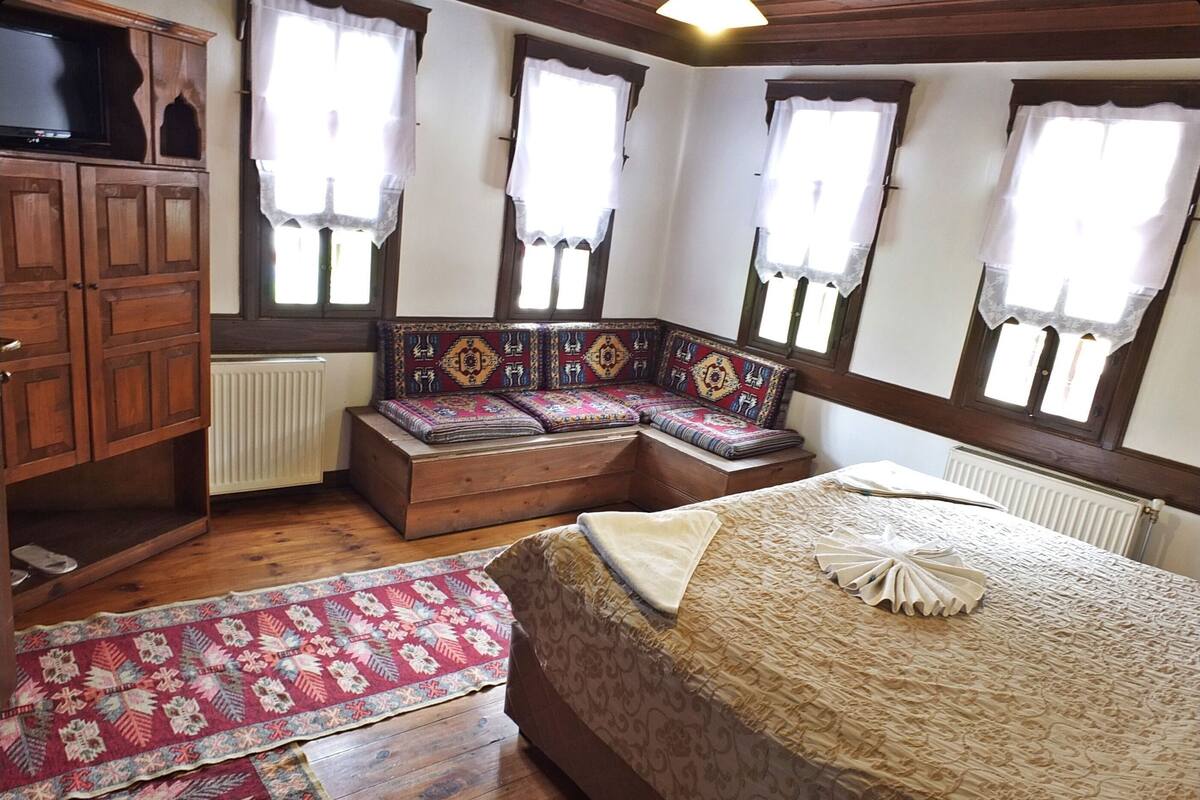 A bedroom with a bed, a wooden bench, a TV, and a radiator.