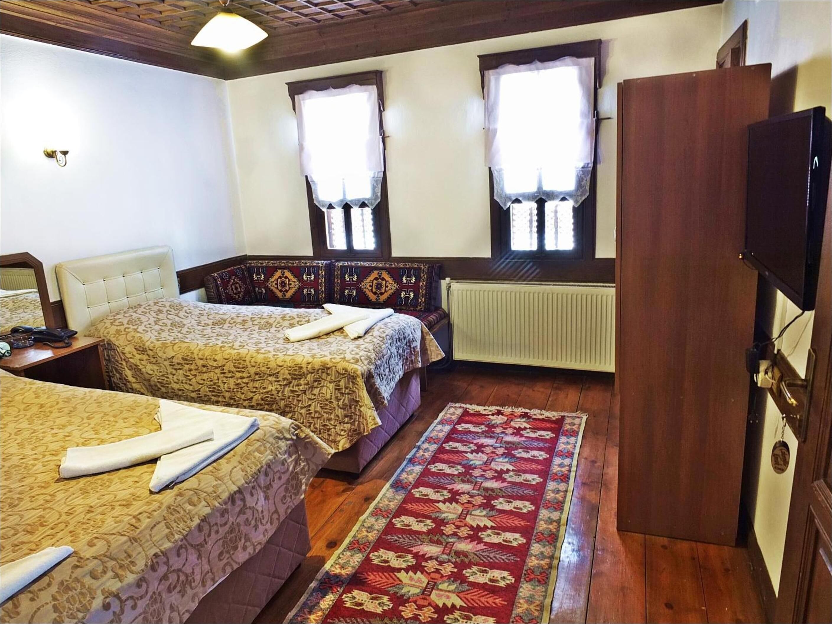 A hotel room with two beds, a wooden wardrobe, a television, and a radiator.