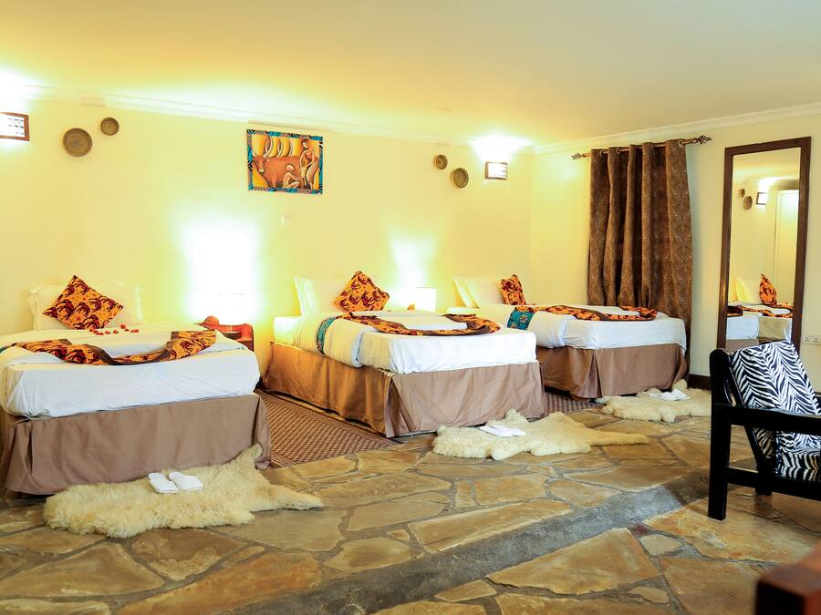 A hotel room with three beds, stone flooring, and a mirror.