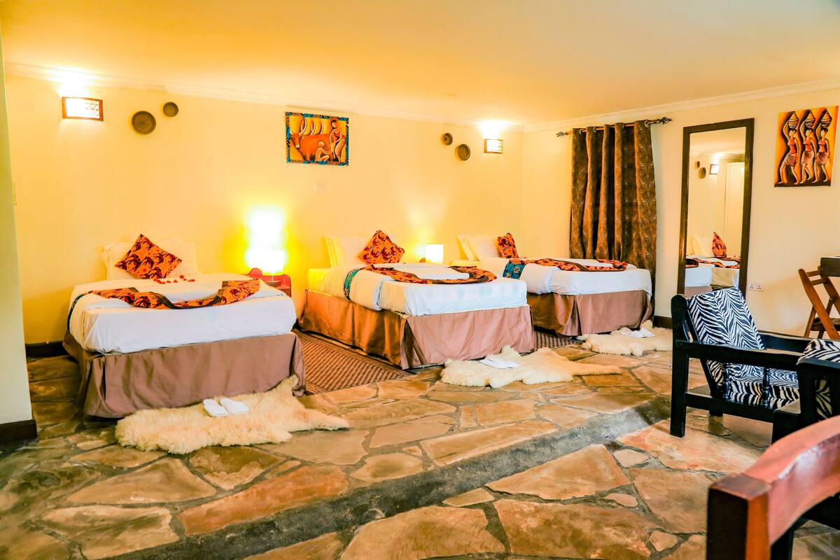 A hotel room with three beds, a stone floor, and a mirror on the wall.