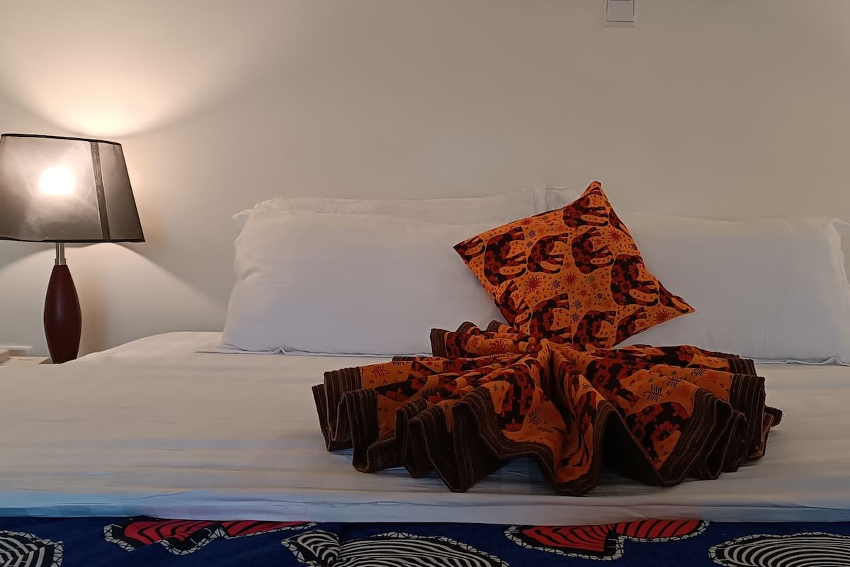 A hotel room with a bed, two bedside lamps, and a patterned throw blanket.