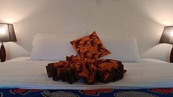 A hotel room with a bed, two bedside lamps, and a patterned throw blanket.
