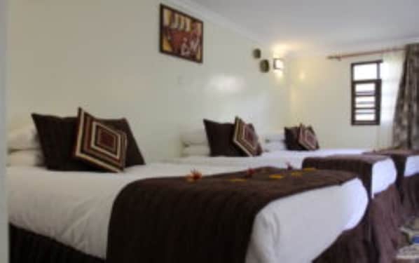 A hotel room with two beds, each with a brown bedspread and multiple pillows. There is a painting on the wall and a window with curtains. - Da Vinci Gorilla Lodge (Kinigi)